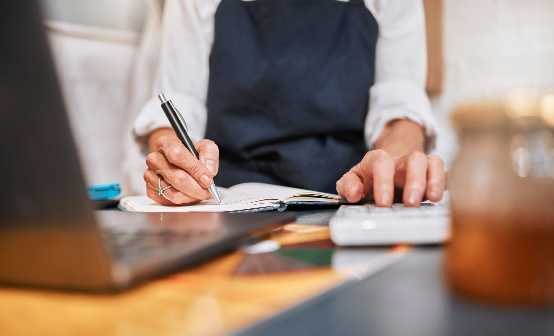 Finance, accounting and hands writing a budget for marketing or advertising a small business startup. Notebook, calculator and entrepreneur working on financial data analysis or sales growth goals